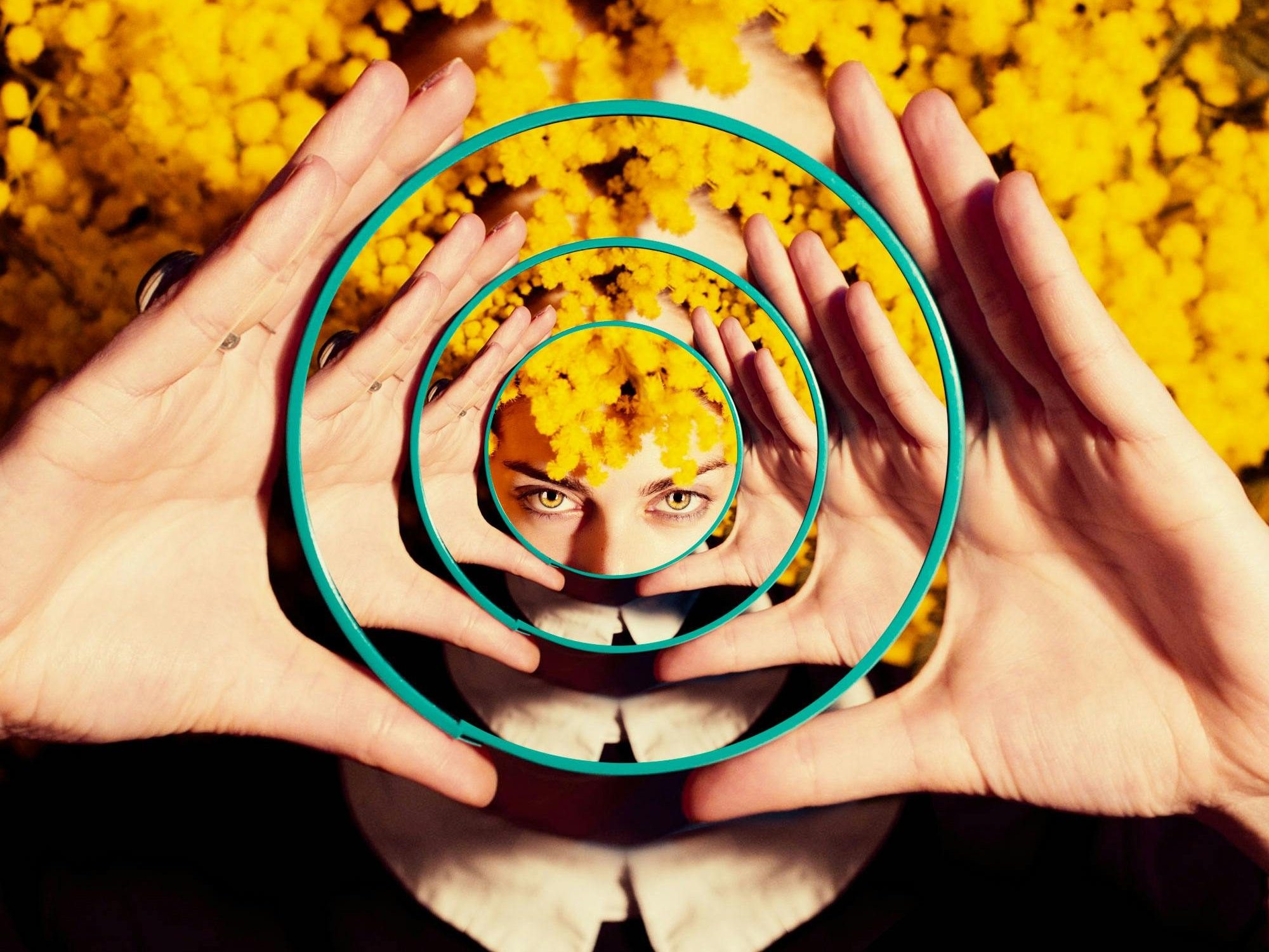 Image of a woman with bright yellow curly hair looking at a reflection of herself as contained within a series of nested circular mirrors